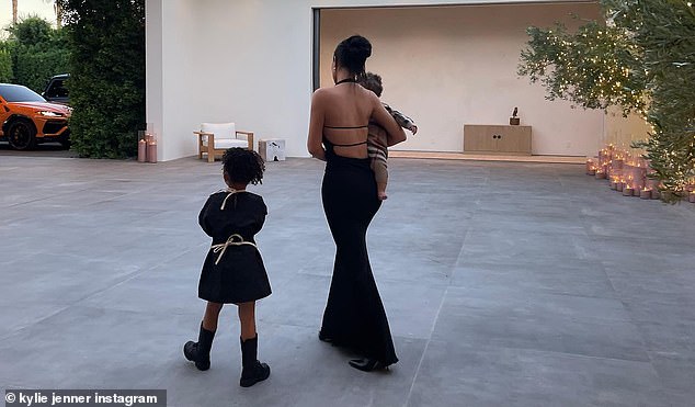 Impresionante: Kylie se veía deslumbrante con un vestido de sirena negro con una blusa sin mangas y espalda escotada mientras caminaba por el patio cargando al bebé, mientras la pequeña Stormi se abrazaba con su vestido festivo.