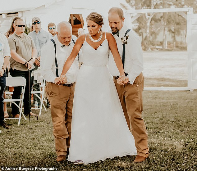 Ally Grizzard, de 23 años, que quedó paralizada de la cintura para abajo después de un accidente automovilístico hace tres años, caminó por el pasillo el día de su boda.  En la foto: Grizzard caminando por el pasillo con su papá y su padrastro sosteniéndola